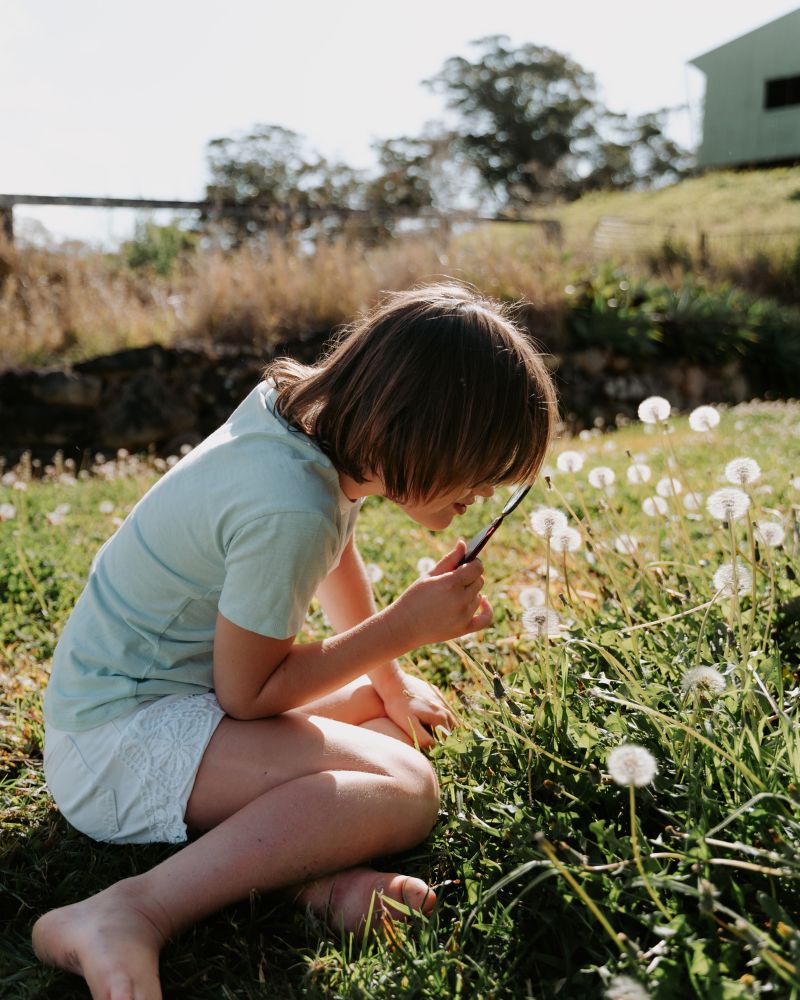 Girl looking through magnifying glass at flowers