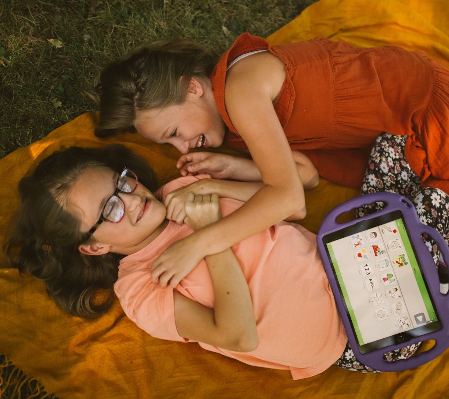 Two girls laying on a blanket with a tablet